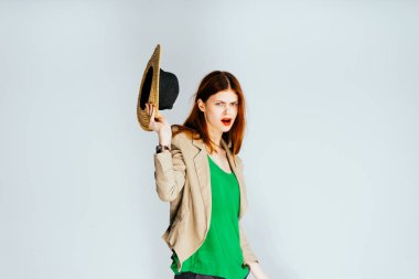 bir kız parlak dudaklar ve yeşil bir bluz onun şapkasını alır ve onun elinde tutan ve izole kameraya benziyor