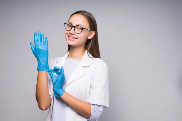 Bella ragazza con gli occhiali e un cappotto bianco indossa guanti di gomma blu e sorride e guarda la fotocamera, isolato — Foto Stock