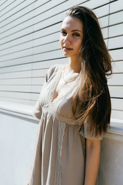 Hermosa linda chica con el pelo largo y en un vestido beige en una calle de la ciudad mira a la cámara — Foto de Stock