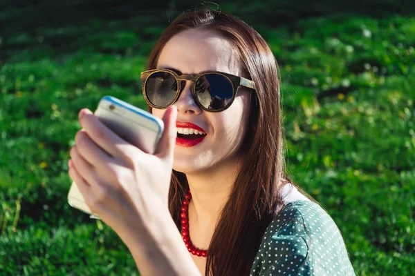 Una donna che fa selfie. bella ragazza in occhiali da sole è seduto sull'erba — Foto Stock
