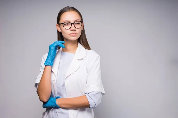 Buena chica con gafas y una bata blanca y guantes seriamente mirando hacia otro lado, aislado — Foto de Stock