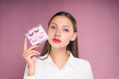 genç güzel kız Beyaz gömlekli onun elinde bir sürü sahte kirpik tutar.