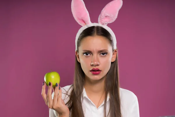 Szomorú lány szép ajkak és rózsaszín fülek, a fején a zöld alma tart a kezében, és néz a kamerába — Stock Fotó