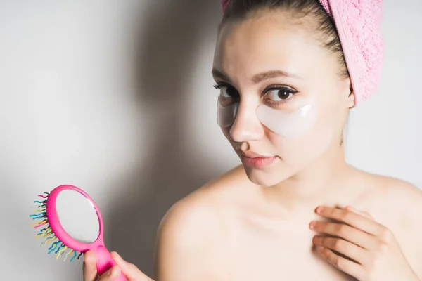 Fille après douche avec une serviette rose sur la tête avec des patchs sur son visage tenant un peigne et regardant la caméra — Photo