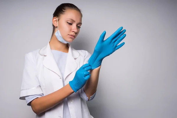 Una ragazza triste con un cappotto bianco e indossando una maschera indossa i guanti. Isolato su sfondo bianco — Foto Stock