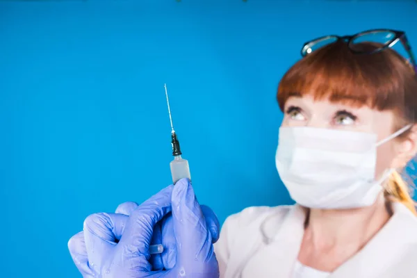 The red-headed nurse in the mask is going to inject a patient. close-up syringe