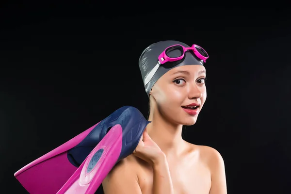 Веселая девушка в плавательной кепке и с ластами в руках собирается купаться в бассейне. Изолированный на черном фоне — стоковое фото