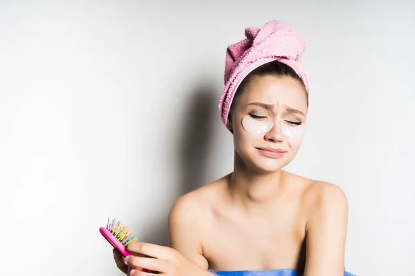 Flickan efter duschen med en rosa handduk på huvudet med fläckar på hennes ansikte drar ut håret från kammen och vrider ansiktet — Stockfoto