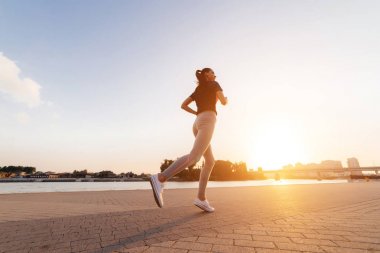kulaklıklar müzik dinlemek nehir dolgu üzerinde koşu spor kıyafetli kız. günbatımı 
