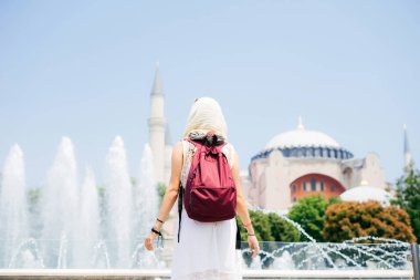 Bir eşarp ile cami ve Çeşme bir arka plan üzerine bir sırt çantası içinde tanınmayan bir kadın. Yaz tatili, gezgin