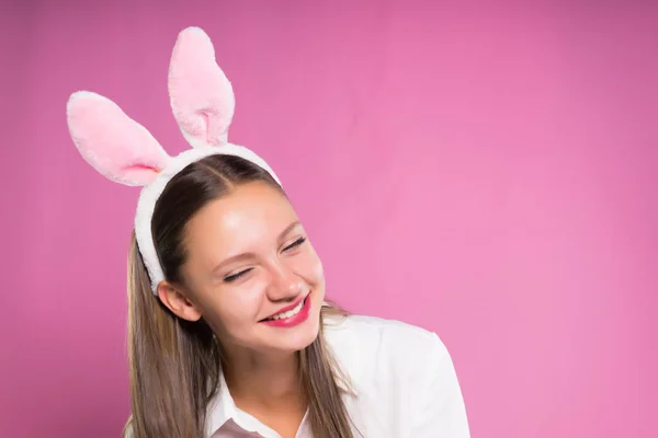 Una ragazza divertente con le orecchie di lepre sulla testa ride. su fondo rosa, isolato — Foto Stock