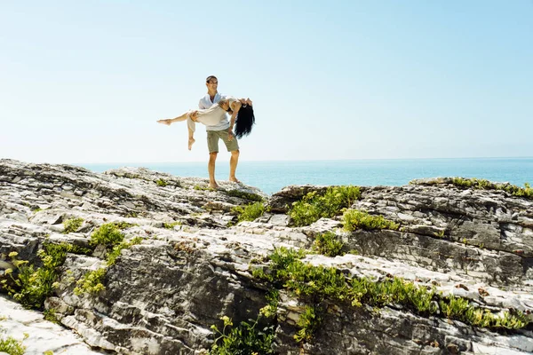 Un uomo tiene una ragazza tra le braccia in lontananza sullo sfondo dell'oceano — Foto Stock