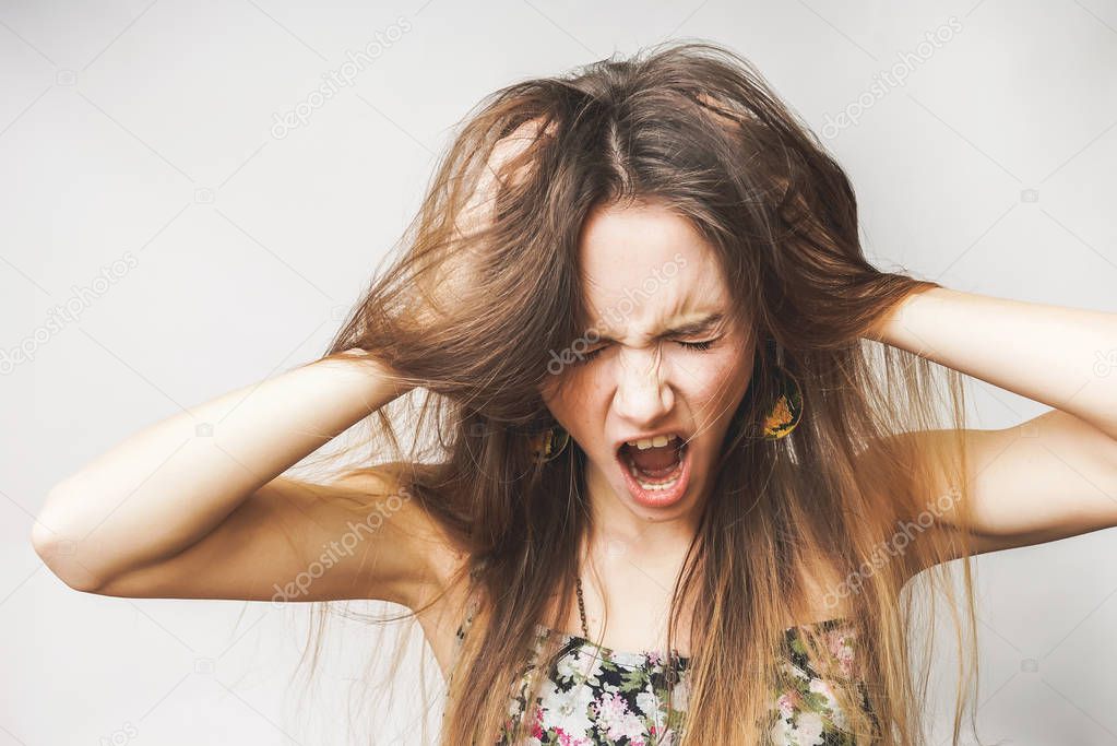 a young angry girl holds her head, shouts, her hair is disheveled