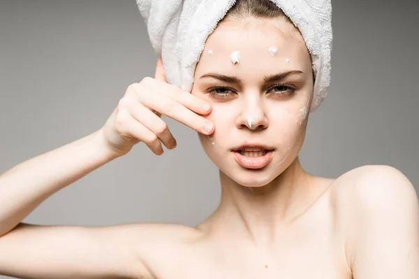 Jovem menina confiante com toalha branca na cabeça aplicando creme no rosto — Fotografia de Stock