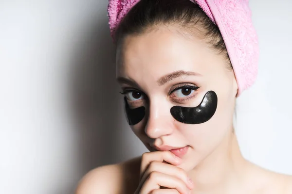 Красивая девушка с чистой кожей, с розовым полотенцем на голове и черными силиконовыми пятнами под глазами, смотрит в камеру — стоковое фото