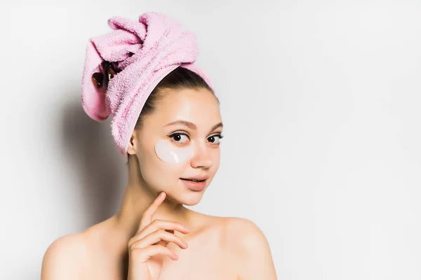 Hermosa chica encantadora con una toalla rosa en la cabeza y parches de silicona bajo los ojos posa — Foto de Stock