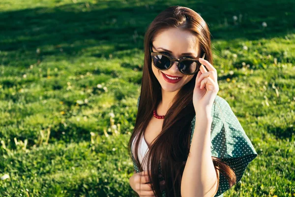 Bella donna su sfondo erba, occhiali da sole, sorriso, intorno all'erba verde — Foto Stock