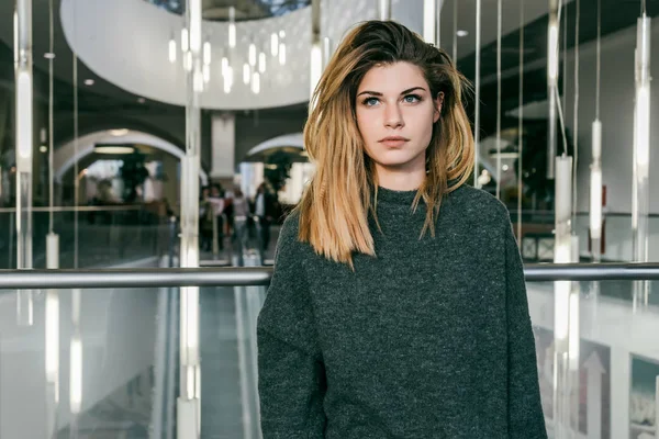 Bela menina elegante com cabelo grosso sentado perto de uma parede de vidro, olhando para longe — Fotografia de Stock