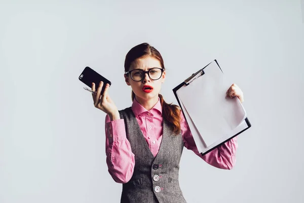Élégante fille en colère avec des lunettes, avec du rouge à lèvres tient un smartphone et des documents dans ses mains , — Photo