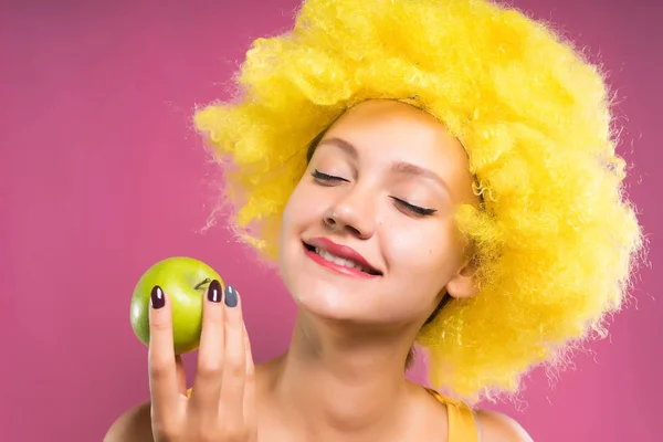 Rolig tjej i gula clown peruk holding ett äpple i hennes hand, leende — Stockfoto