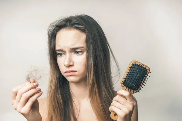 Молодая грустная девушка, держа в руке деревянную расческу и расчесывая волосы — стоковое фото