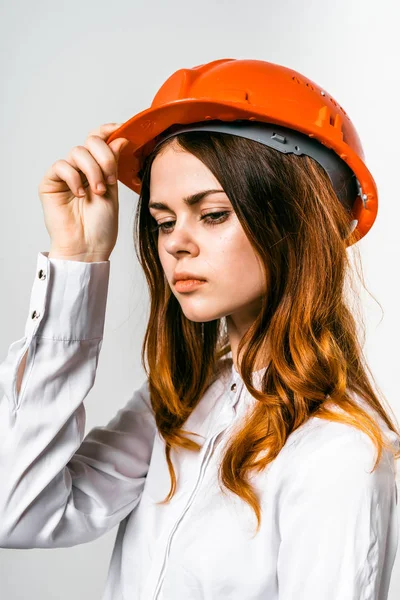 Chica joven seria en un casco protector naranja, en una camisa blanca mira hacia abajo — Foto de Stock