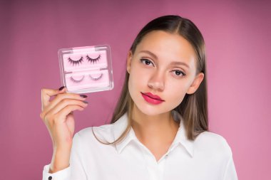 genç güzel kız Beyaz gömlekli onun elinde bir sürü sahte kirpik tutar.