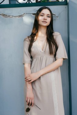 bej renkli elbiseli seksi çekici kız duvara poz güneş gözlüğü onun elinde tutan