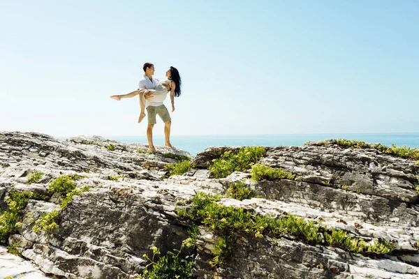 Un uomo tiene una ragazza tra le braccia in lontananza sullo sfondo dell'oceano — Foto Stock