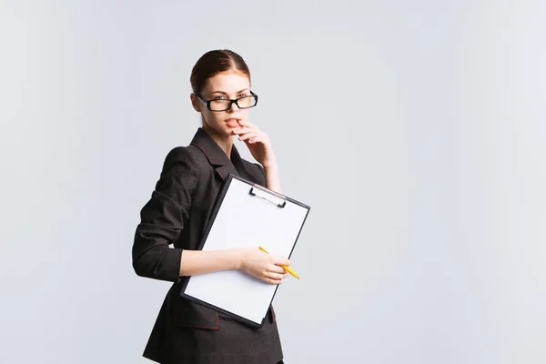 Строгая рыжая девушка в очках и черном медицинском костюме держит документы в руке, глядя в камеру — стоковое фото