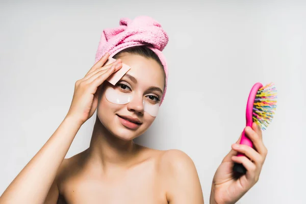 Молодая девушка с розовым полотенцем на голове, держит расческу, вытирает лицо, улыбается — стоковое фото
