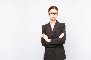 ciddi bir genç kız bir takım elbise ve gözlük duruyor, kollarını göğsüne katlanmış, kameraya doğru görünüyor