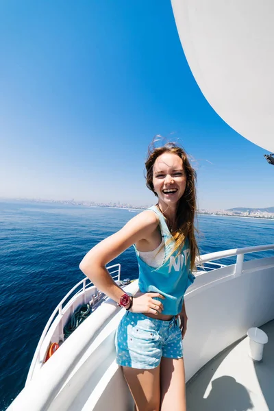 happy girl in blue clothes is standing on a white yacht, laughing, around a blue ocean