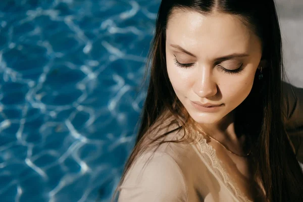 Сексуальная девушка сидит у голубой воды, наслаждается солнцем — стоковое фото