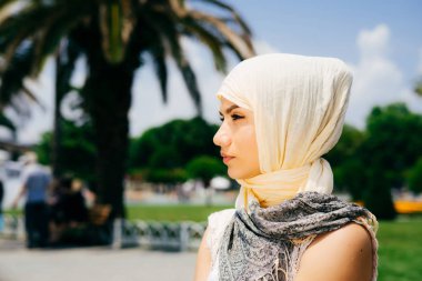 Güzel genç modern Müslüman kadın ve palmiye ağaçlarının fonunda bir yaz parkta oturan bir eşarp