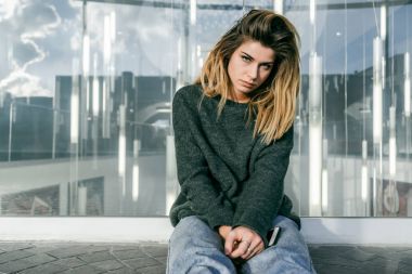 kalın saçlı bir cam duvara yakın oturan üzgün şık kız
