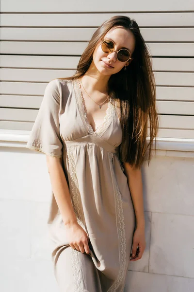 Mooie charmante meisje in een beige jurk en zonnebril poseren in de zon — Stockfoto