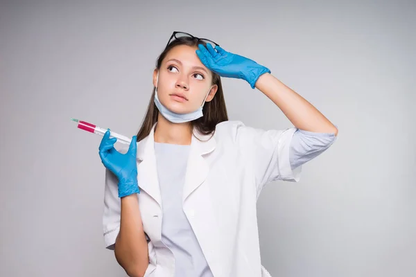 Giovane donna intelligente medico in vestaglia medica bianca tiene una siringa tra le mani, sembra stanco — Foto Stock