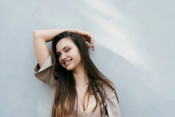 Chica sexy feliz en un vestido beige posando junto a una pared de luz, riendo — Foto de Stock