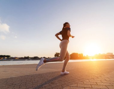 günbatımı kulaklıklar müzik dinlemek, nehrin etrafında koşan genç atletik atlet kız