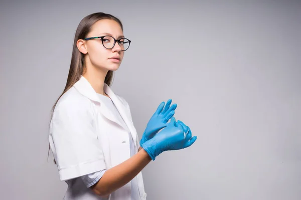Ung självsäker tjej läkaren i vit medicinsk klänning och glasögon tar bort blå handskar — Stockfoto
