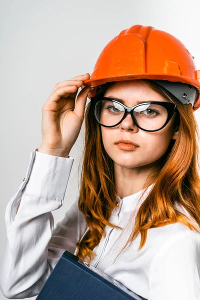 Jovem menina bem sucedida com óculos e um capacete protetor laranja olha com confiança para a câmera — Fotografia de Stock