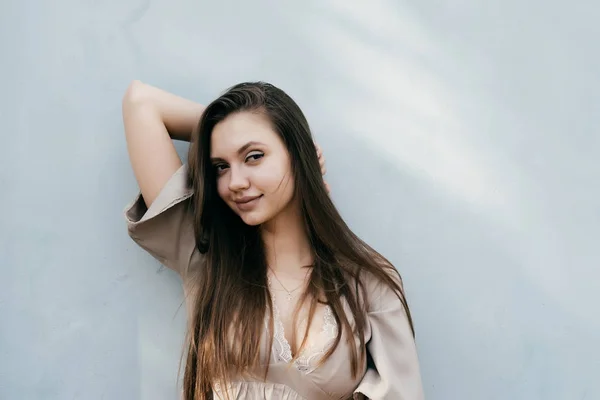 Sexy attractive long-haired girl posing by a light wall — Stock Photo, Image