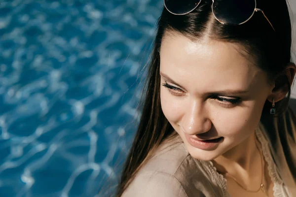 Sexy atractiva chica de pelo largo sentado cerca de agua azul en el sol, sonriendo — Foto de Stock