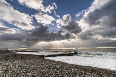 çakıl plajdan denize, beyaz köpük dalgalardan rages, güneş tarafından gri bulutlar kaplı