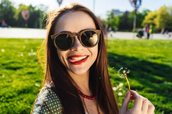Divertente sorridente donna felice in occhiali da sole che soffia dente di leone — Foto Stock