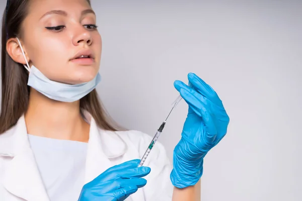 Inteligente médico joven con una bata médica blanca y guantes azules sostiene una jeringa con una solución médica en el interior — Foto de Stock