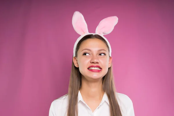 Een grappig meisje in een wit overhemd en de rand in de vorm van de oren van het konijn writhes een grappig gezicht — Stockfoto