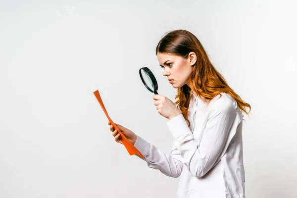 Menina inteligente na camisa branca olha para documentos através de lupa — Fotografia de Stock