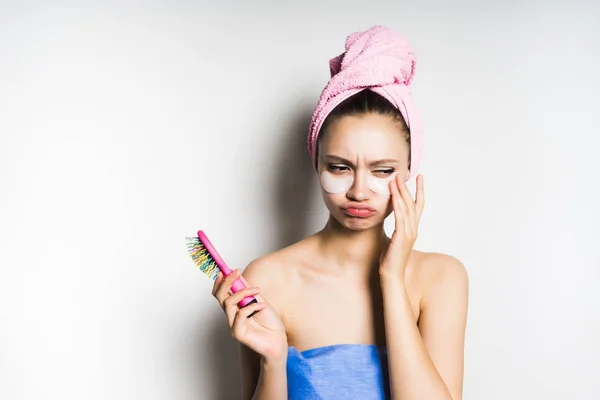 Sorgsen ung flicka med rosa handduk på huvudet, silikon fläckar under ögonen håller en rosa hårkam — Stockfoto